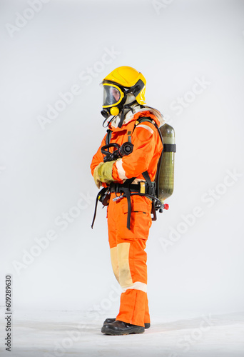 Side view of firefighter wearing yellow hard hat standing holding fire hose with both hands on white background.