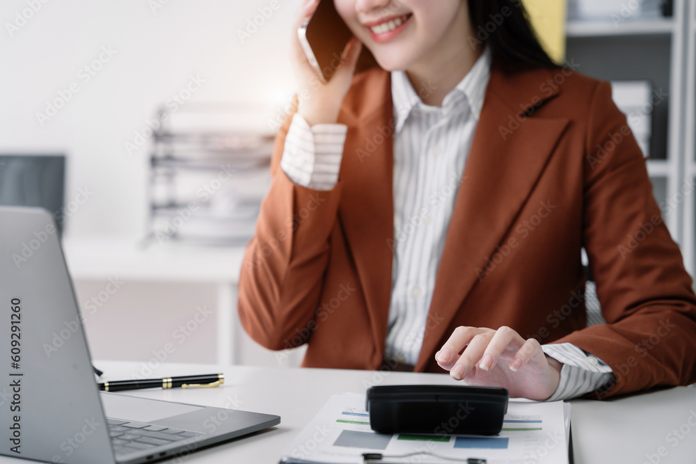 Asian woman talking on mobile phone and working on laptop and calculator on table in office. Asian woman talking on mobile phone and working on laptop and calculator on table in office.