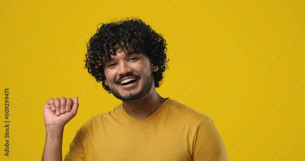 Young indian man waves hand palm in hello gesture welcomes someone expresses positive emotion standing over orange studio background Young indian man waves hand palm in hello gesture welcomes someone expresses positive emotion standing over orange studio background