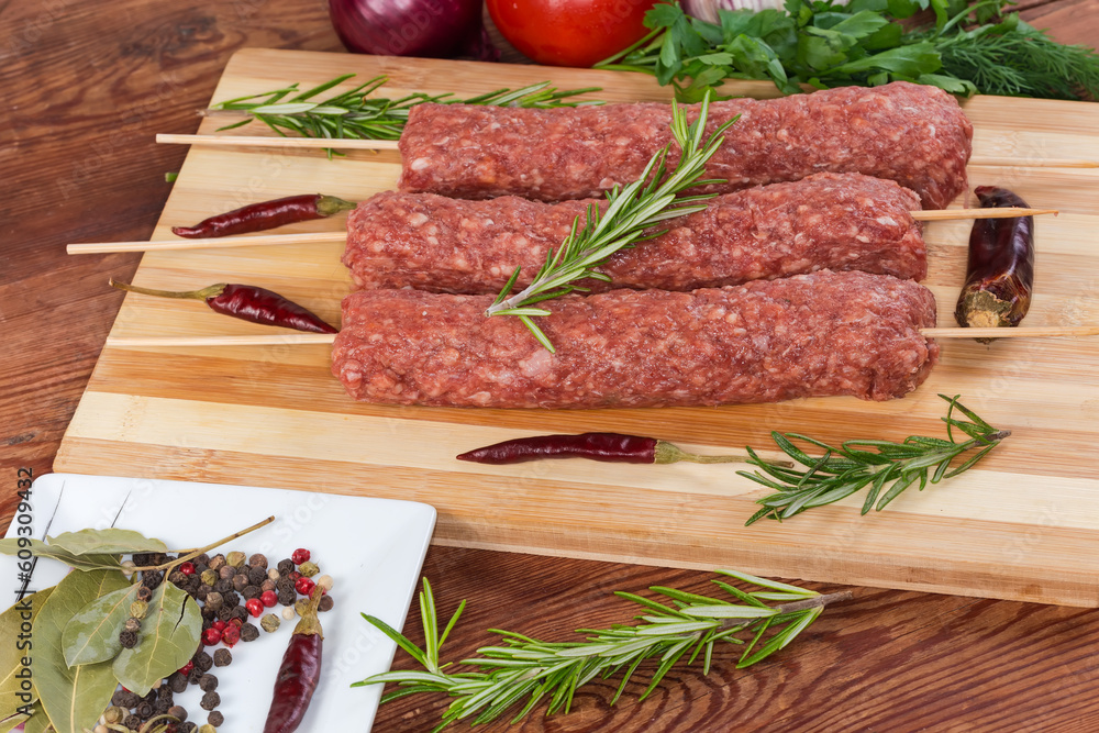 Raw lula kebab on cutting board among vegetables and spices