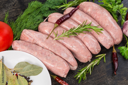 Raw sausages among the spices and greens on black surface