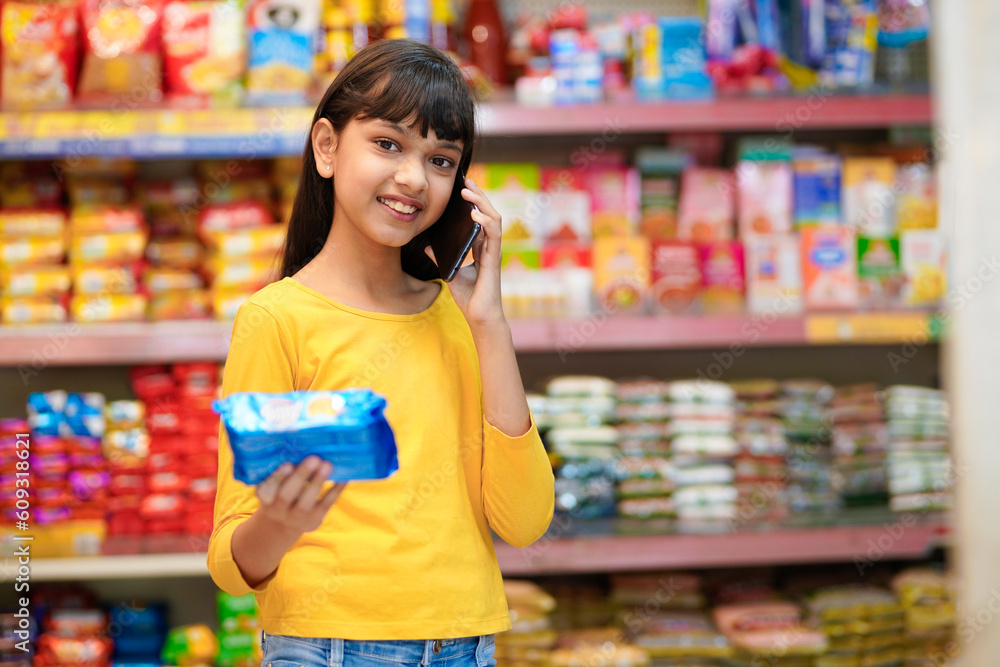 Indian girl talking on smartphone at grocery shop.