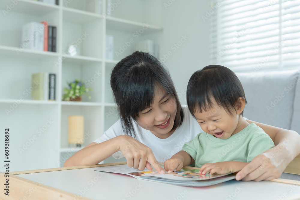 Happy Asian mother relax and read book with baby time together at home. parent sit on sofa with daughter and reading a story. learn development, childcare, laughing, education, storytelling, practice. Happy Asian mother relax and read book with baby time together at home. parent sit on sofa with daughter and reading a story. learn development, childcare, laughing, education, storytelling, practice.