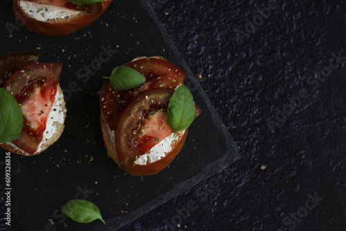 Bruschetta with cheese and red and black tomatoes with basil on a dark background