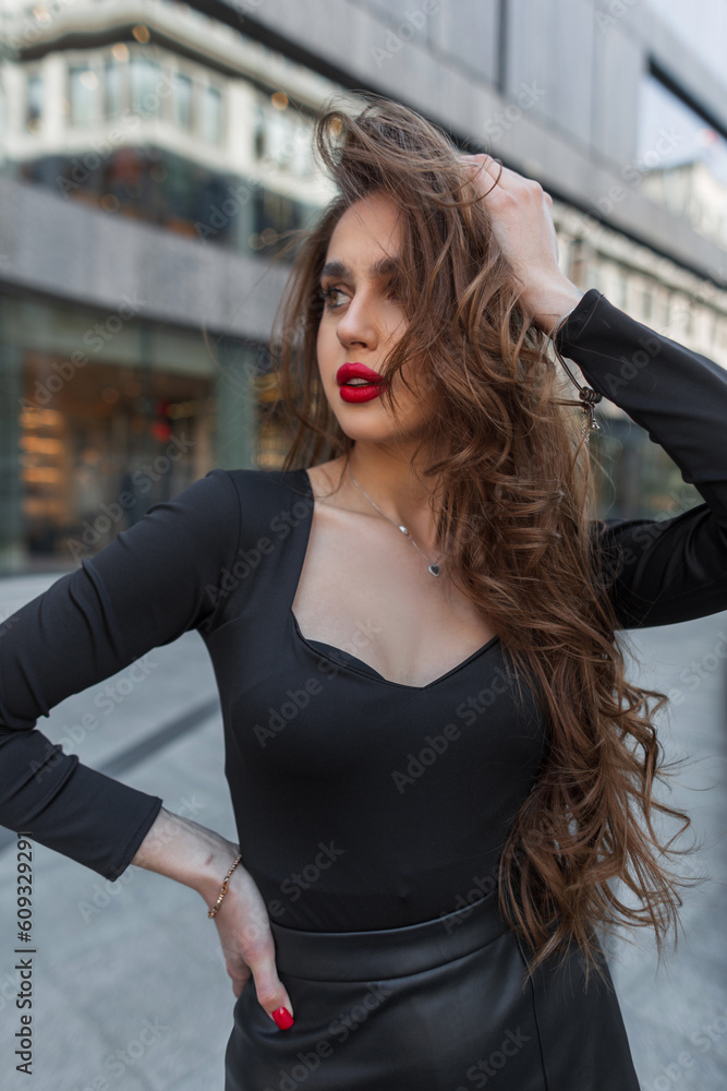 Gorgeous beautiful fashion brunette girl with red lips in elegant clothes walks in the city and straightens her hair