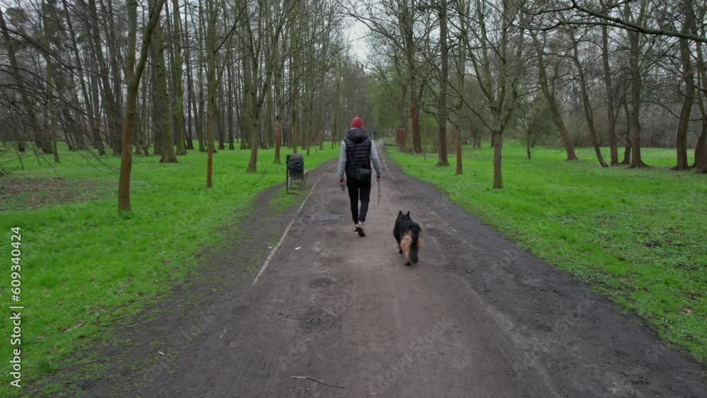 It's the beginning of spring, a man in a cap and vest walks his dog in a park, the cloudy sky above. It's the beginning of spring, a man in a cap and vest walks his dog in a park, the cloudy sky above.