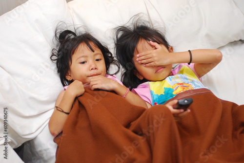 two beautiful Asian girls watching TV in the room while scared