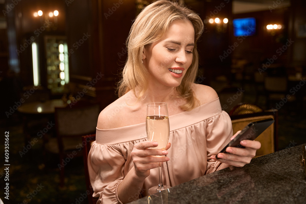 Smiling lady texting with her boyfriend with glass of champagne at bar - obrazy, fototapety, plakaty 