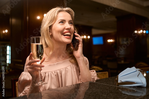 Smiling lady talking on phone while sitting at bar counter