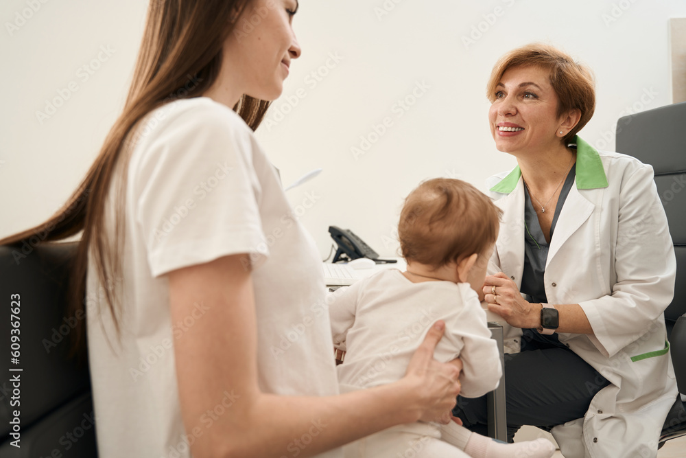 Obraz premium Friendly ophthalmologist giving primary consultation to young mother with infant
