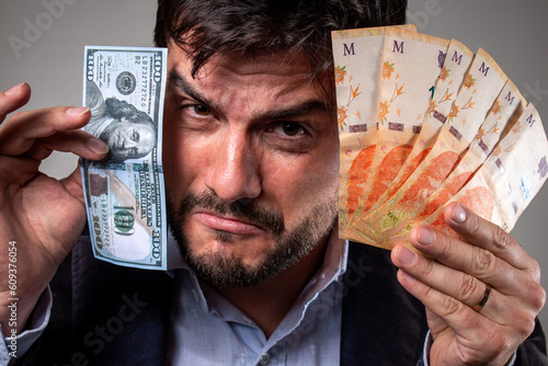 Hombre triste por la devaluación sosteniendo pesos argentinos y un billete de 100 dolares photo