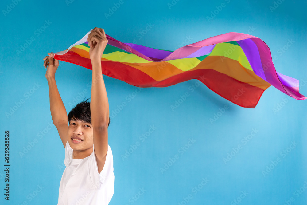 Young gay man holding colorful rainbow flag on blue color background ...