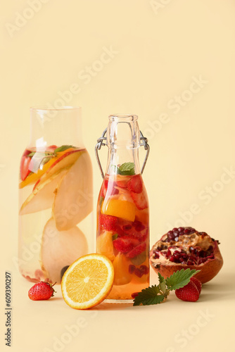 Bottles of infused water with different sliced fruits on beige background