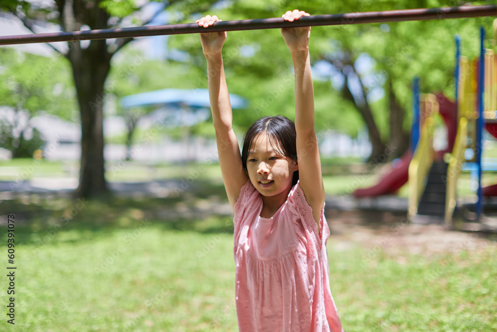 夏の公園で鉄棒を遊んでいる小学生の女の子の様子