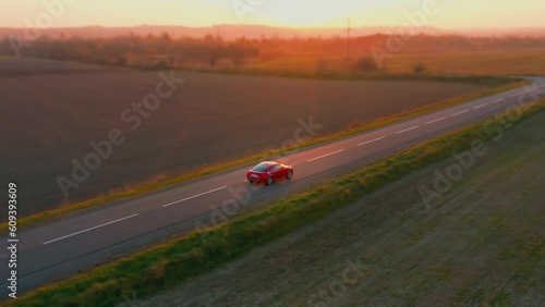 Aerial shot of a red car driving along an asphalt highway road.