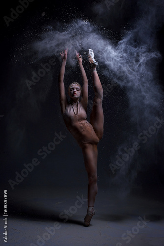 Ballerina Jumping, Modern Ballet Dancer in Pointe Shoes, Black Background, Woman is dancing, a cloud of flour is around her. On hair at the woman white flour, it scatters dust about the room.