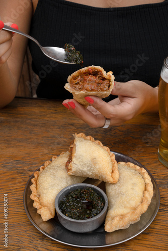 Eating empanadas at the restaurant. Closeup view of a caucasian woman having fried meat empanadas with traditional chimichurri sauce.