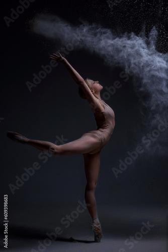 Ballerina Jumping, Modern Ballet Dancer in Pointe Shoes, Black Background, Woman is dancing, a cloud of flour is around her. On hair at the woman white flour, it scatters dust about the room.