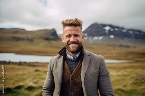 Handsome bearded man smiling and looking at camera while standing on the edge of a mountain in Iceland