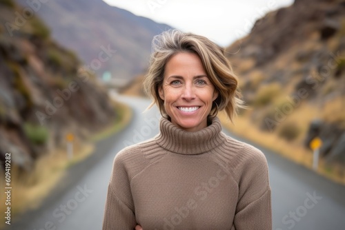 Medium shot portrait photography of a pleased woman in her 40s that is wearing a cozy sweater against a mountain pass or winding road background . Generative AI