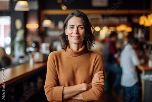 Portrait of smiling businesswoman standing with arms crossed in coffee shop