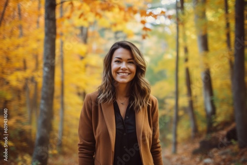Medium shot portrait photography of a grinning woman in her 30s that is wearing a classic blazer against a brilliant display of fall foliage in a forest background . Generative AI