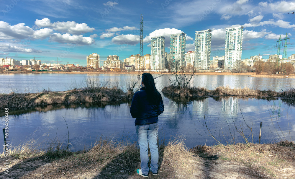 Fototapeta premium A woman stands on the shore of the lake and looks at the city on the other side