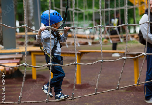 Summer. A small child climbs in a rope park on a rope bridge. A boy is having fun in an Adventure Park. A male baby on a climbing frame. Compliance with safety techniques.