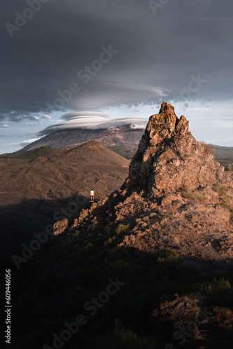 Person standing on a spectacular rock observing the lenticular clouds over the Teide volcano in Tenerife during his adventure through the Canary Islands