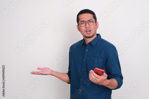 Adult Asian man showing confused expression while holding a mobile phone photo
