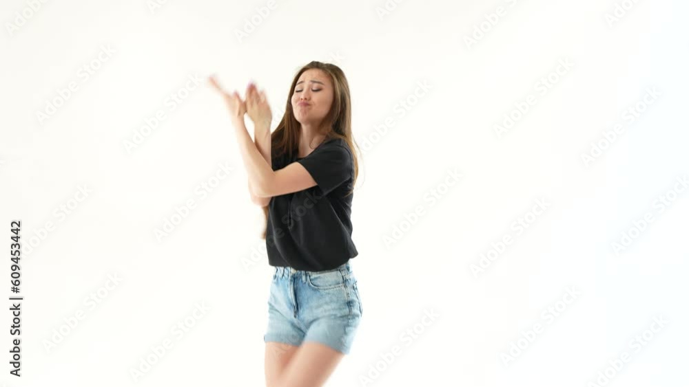 Young Asian woman dancing on white background. She has long hair and wearing short denim shorts and black T-shirt. Joyful girl enjoying her favorite music.