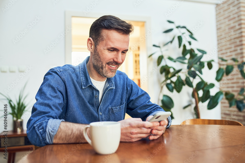 Smiling adult man at home sitting at table using smart phone Smiling adult man at home sitting at table using smart phone