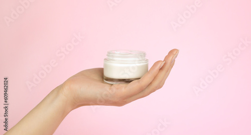 A jar with cream in a woman's hand on a pink background. Layout for advertising a cosmetic brand.