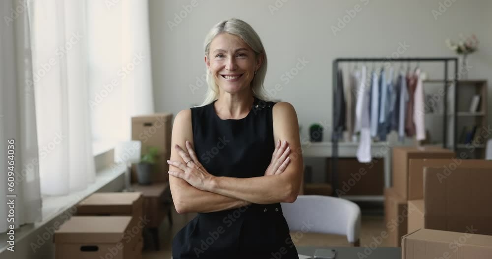 Cheerful confident property buyer woman posing with cardboard relocation boxes in new apartment, looking at camera with happy smile and arms folded, smiling. Home owner portrait Cheerful confident property buyer woman posing with cardboard relocation boxes in new apartment, looking at camera with happy smile and arms folded, smiling. Home owner portrait