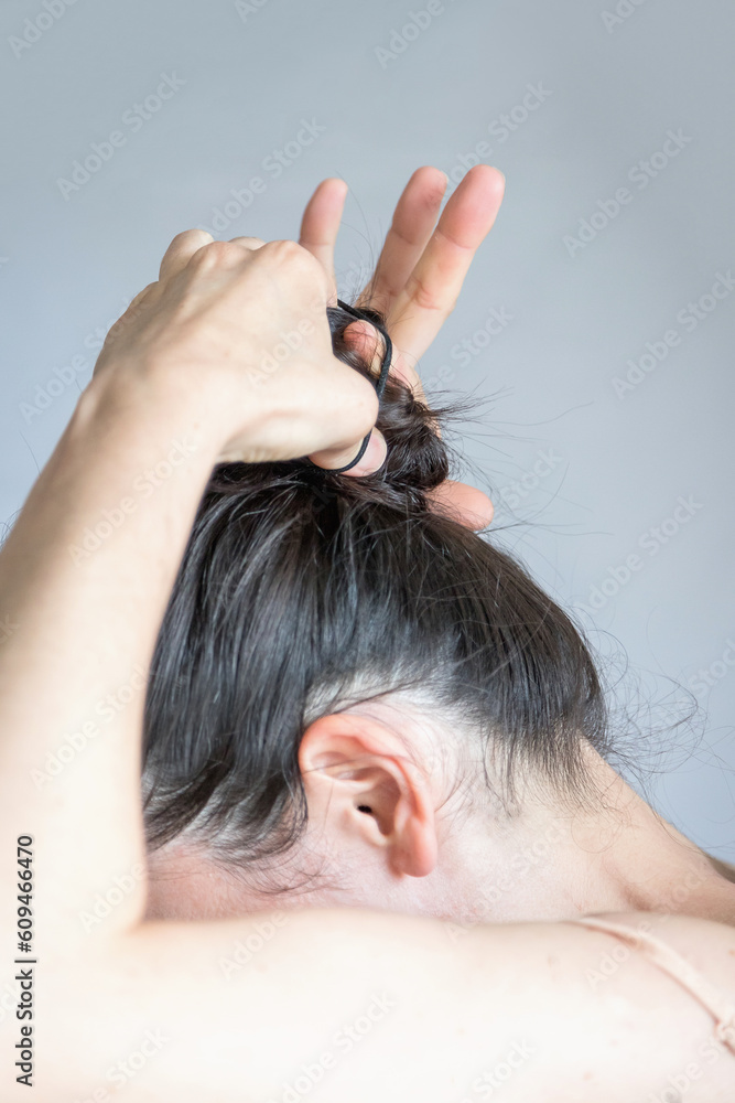 Fototapeta premium Detail of a young caucasian woman making a bun with her hair. Close-up view of a hair routine. Carefree and practical lifestyle concept.