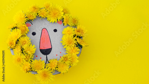 close-up of a lion's head made of cardboard and dandelions on yellow background. children's crafts
