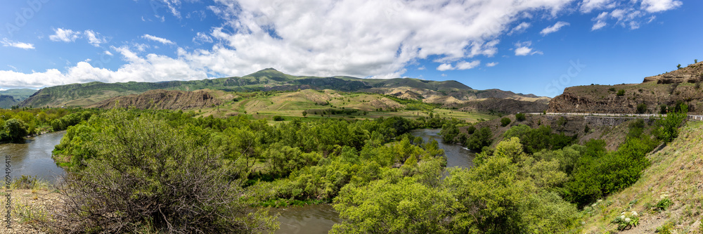 Mtkvari river valley panorama in Samtskhe Javakheti region in Southern Georgia with lush green vegetation and Lesser Caucasus mountains in the background.