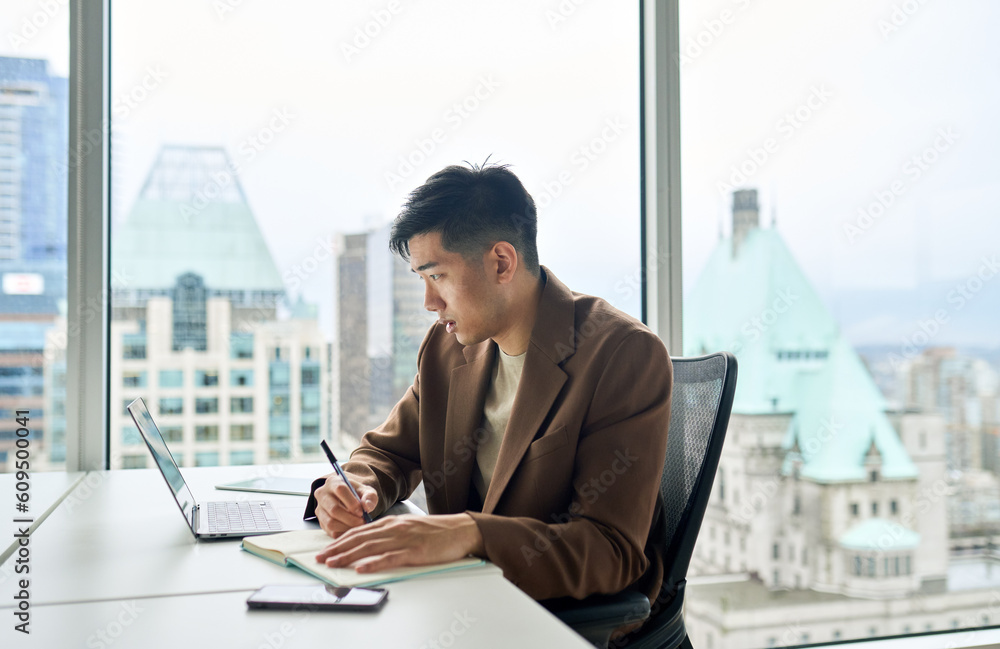 Young busy Asian business man employee working on laptop in corporate office writing notes. Professional businessman company worker using computer, watching webinar, elearning sitting at desk. Young busy Asian business man employee working on laptop in corporate office writing notes. Professional businessman company worker using computer, watching webinar, elearning sitting at desk.