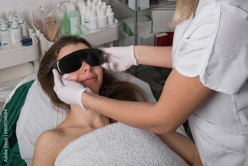 Beautician gives protective eyeglasses for female patient on before laser hair removal procedure