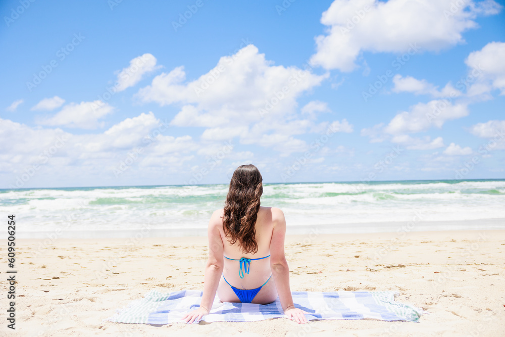 水着でビーチに座るオーストラリア少女の後ろ姿