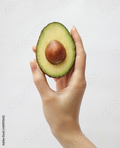female hand holding avocado cut in half isolated on white background