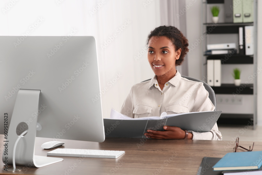 African American intern with folder working at table in office African American intern with folder working at table in office