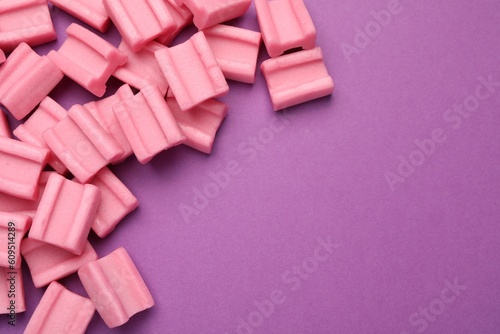 Tasty pink chewing gums on purple background, flat lay. Space for text