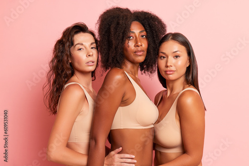 Three girls posing in studio wearing underwear against pink background, black girl standing in middle, Asian one on the left and European girl on the right, diversity concept, copy space © South House Studio
