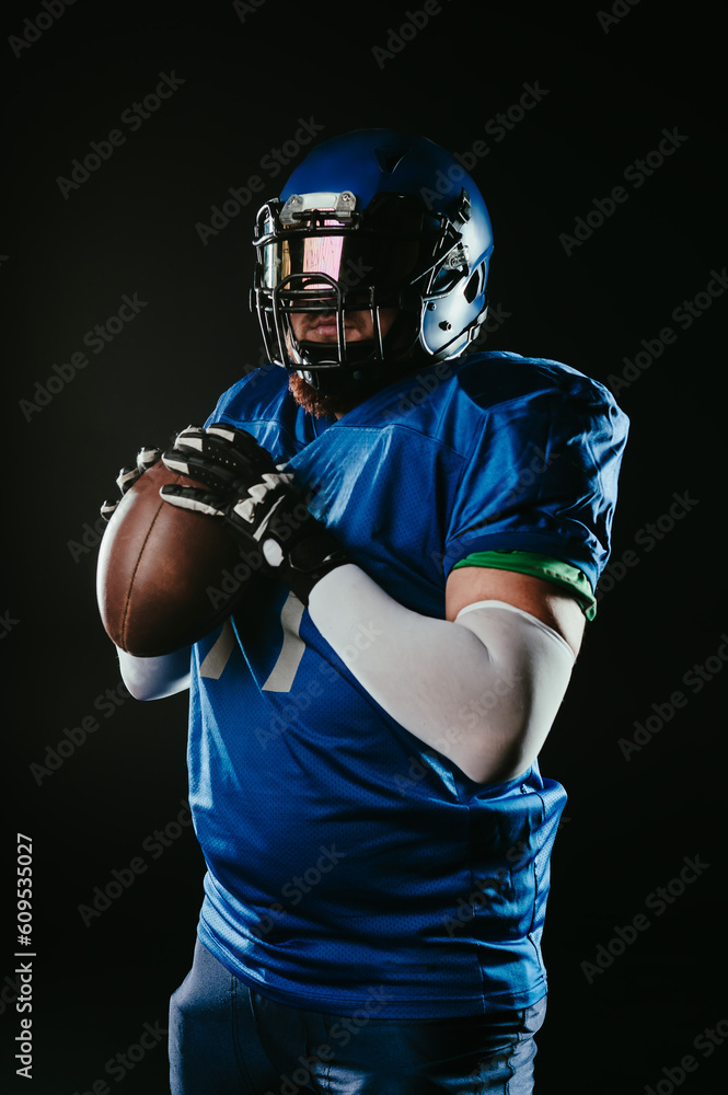 An Asian man with a red beard in a blue American football uniform throws a ball against a black background.