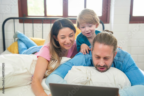 Happy family people leisure in bedroom together. Father and mother with son relaxing and using laptop on bed
