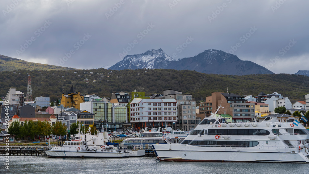 The seaport of Ushuaia. Catamarans and tourist ships are moored in the bay of the Beagle Canal. City houses on the shore. Martial Mountains against a cloudy sky. Argentina.