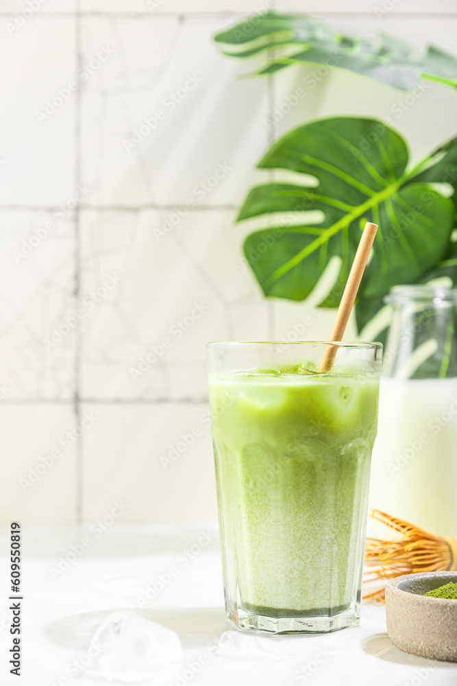 Iced green matcha latte in a glass with milk bottle on white tile background with hard shadows and monstera leaves Iced green matcha latte in a glass with milk bottle on white tile background with hard shadows and monstera leaves