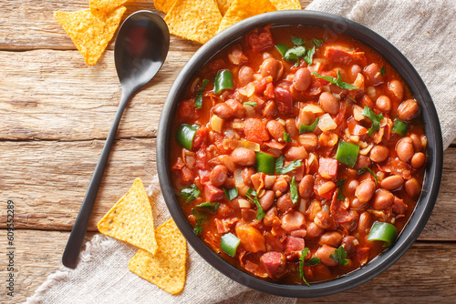 Mexican Charro Beans made with pinto beans, bacon, ham, chorizo, chili peppers, tomatoes and spices closeup on the bowl on the table. Horizontal top view from above photo