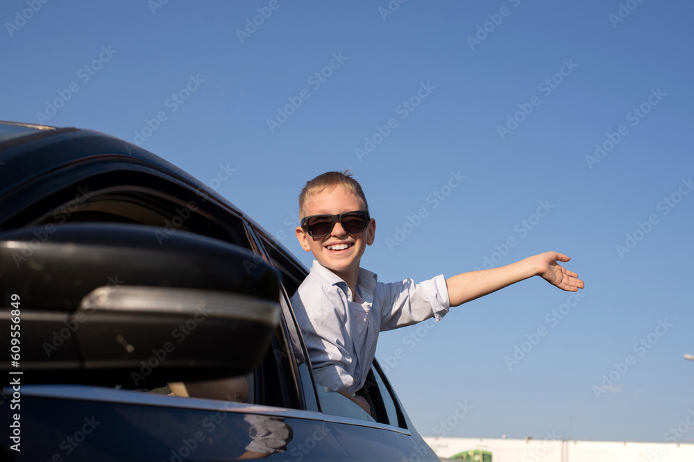 A cute boy in sunglasses looked out of the car window waving his hand with a laugh A cute boy in sunglasses looked out of the car window waving his hand with a laugh